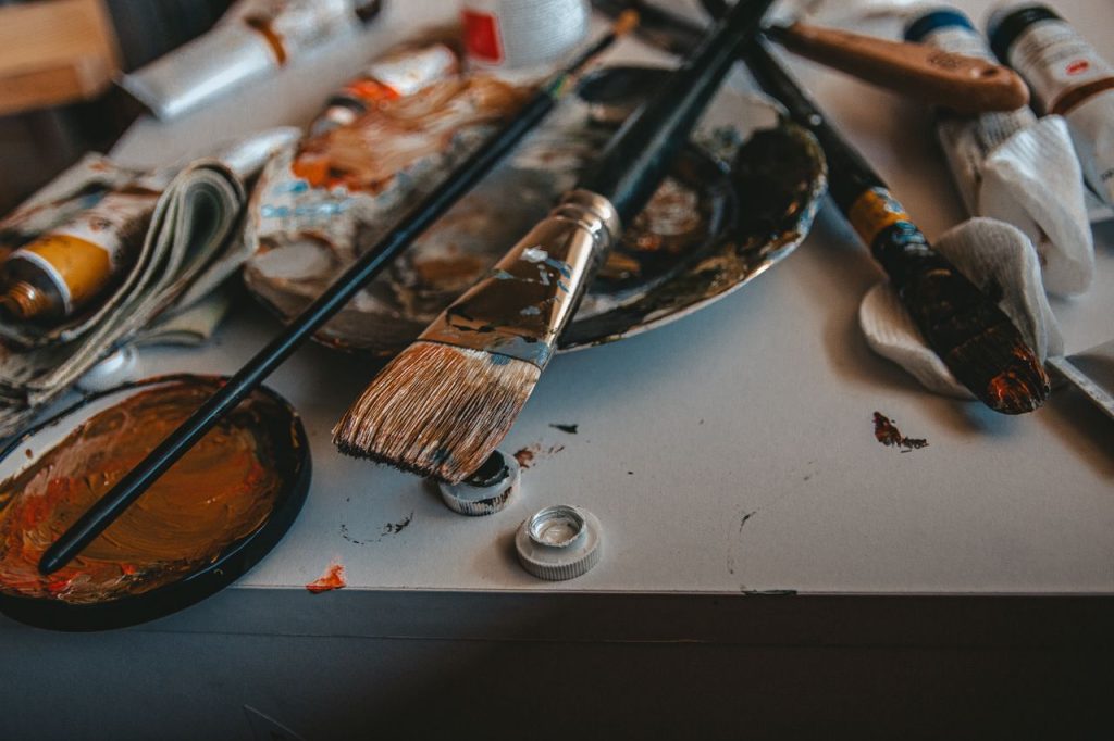 A cluttered artists workspace with paintbrushes and palette, showcasing creativity.