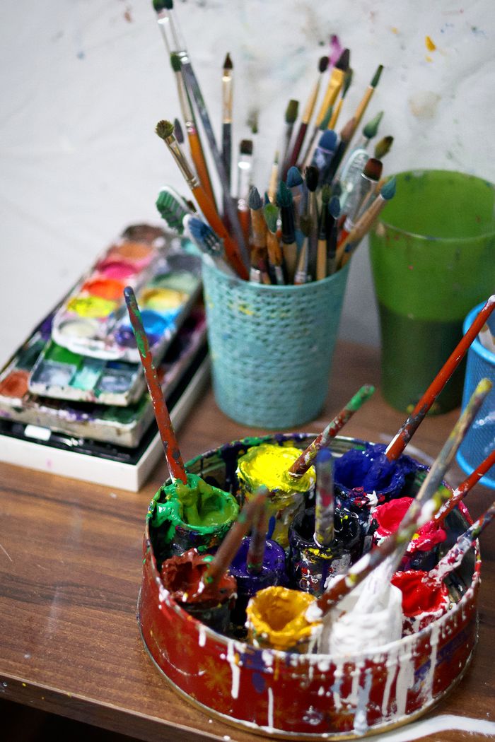 A colorful artists workspace featuring paints, brushes, and a palette.